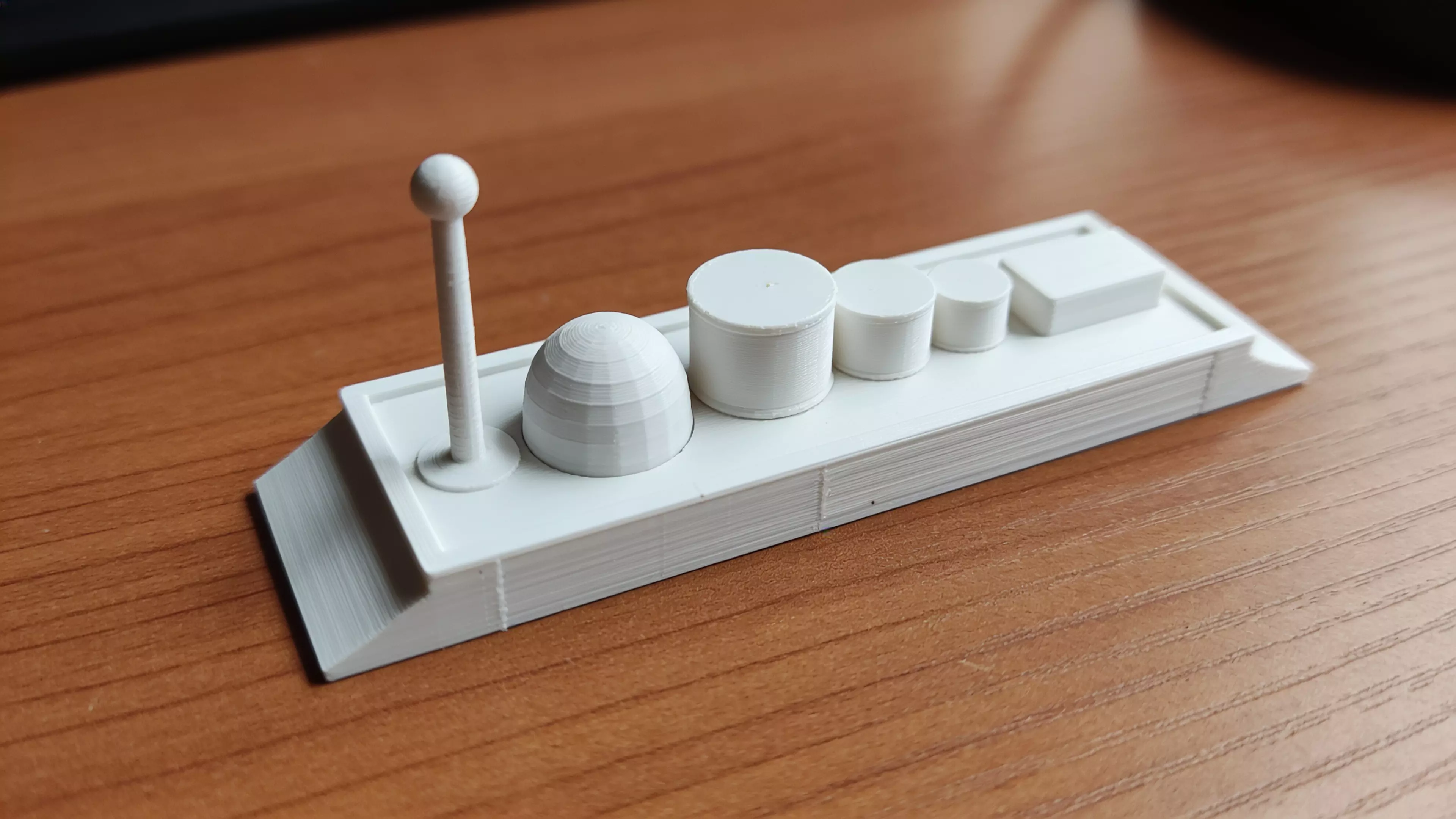 A toy cargo barge — a low, flat-bottomed hull with a raked bow and flat stern — plus six separate deck-cargo pieces (mast/beacon, dome, three drums, and a crate) that peg into sockets on the deck, matching the sketch's assortment.