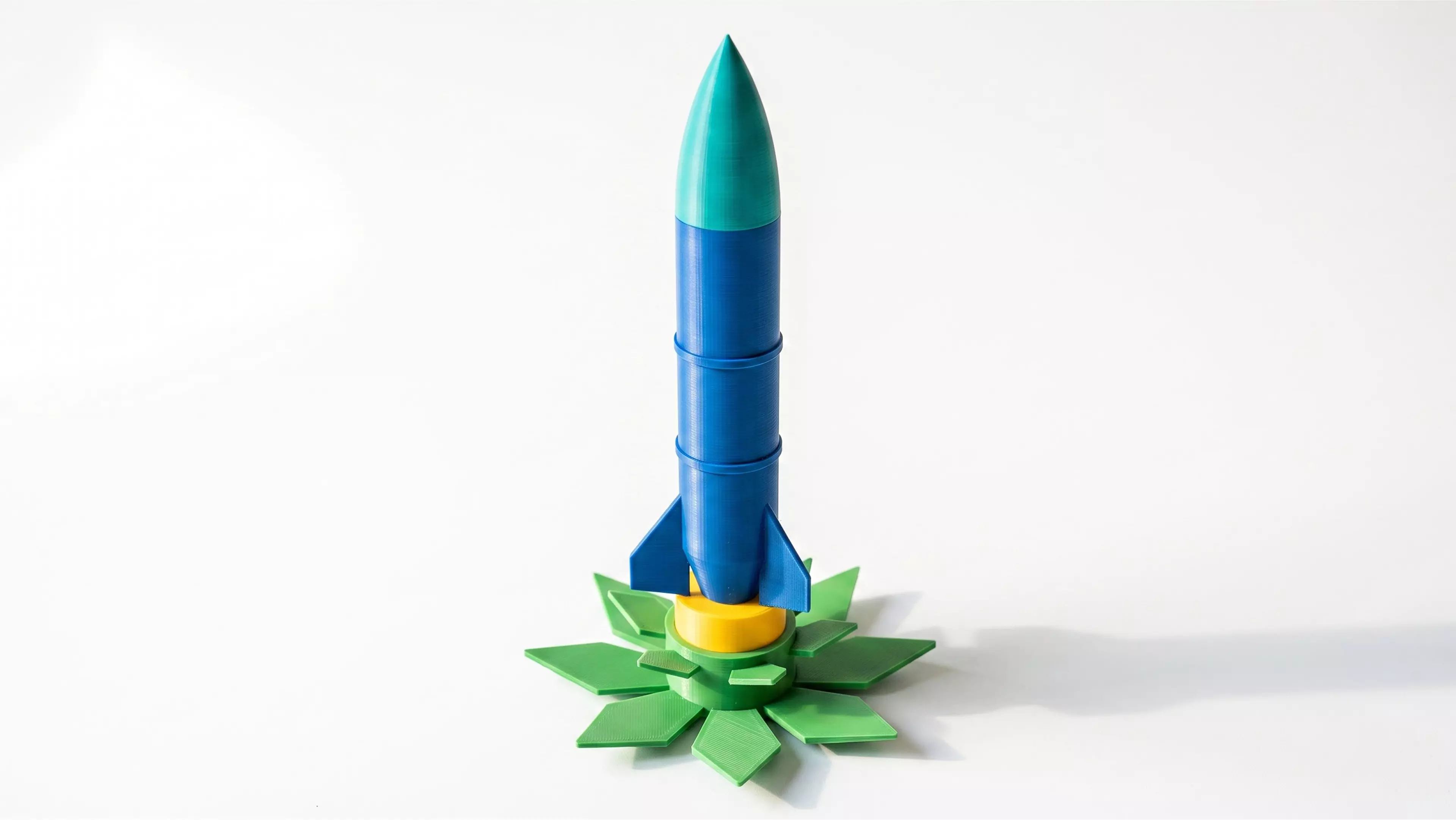 A one-of-a-kind 180 mm-tall display piece: a classic retro finned rocket that plugs into an open-bloom lotus-flower pedestal base — two separate, removable parts, each a different color.