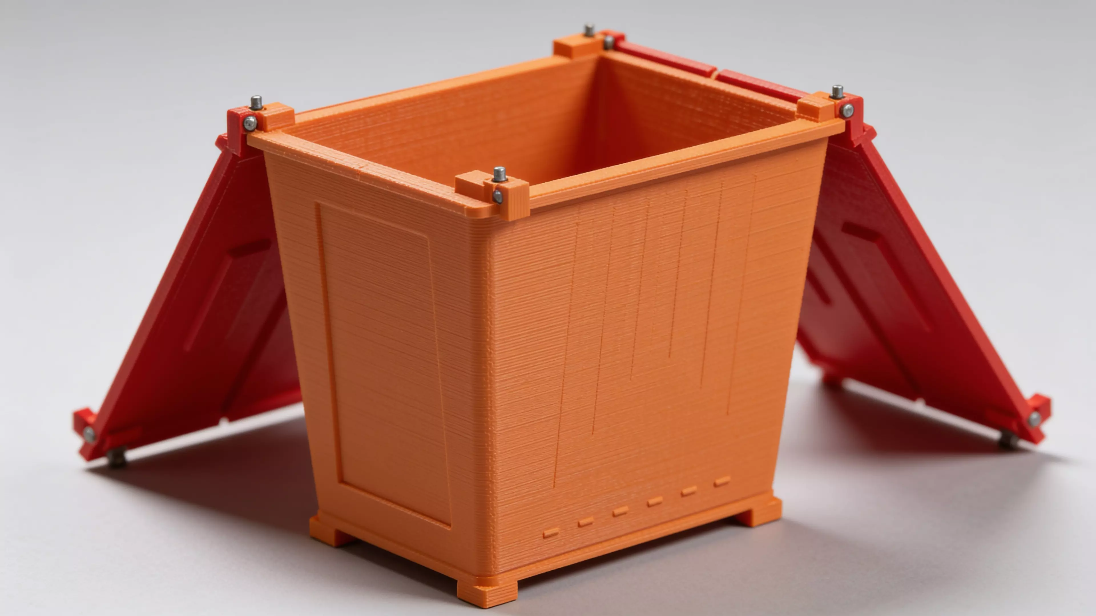 A miniature industrial-dumpster-styled desk trash catcher: a tapered corrugated bin body with two hinged flip lids that meet in the middle, complete with corner skid feet.