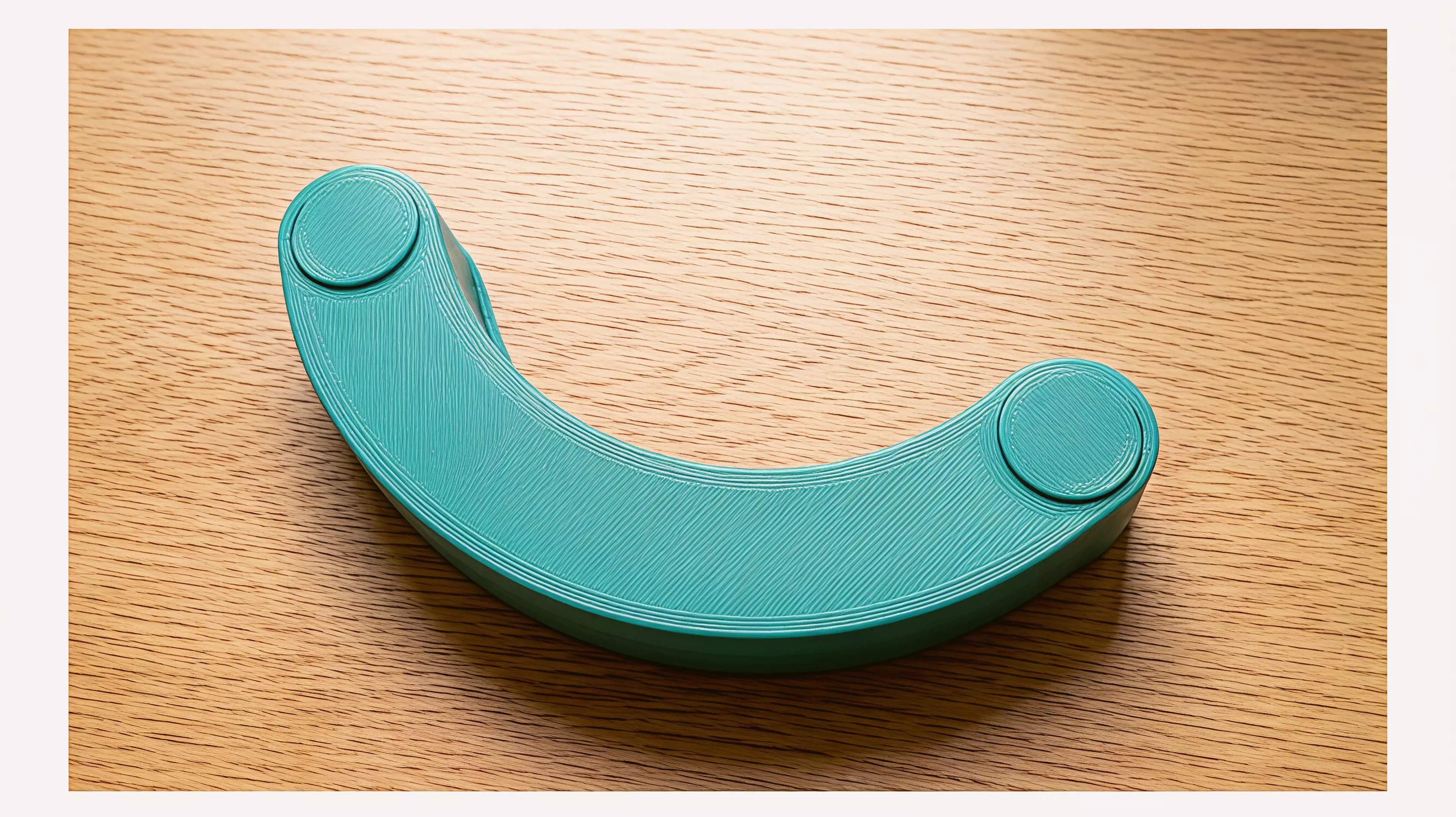 A tiny one-piece crescent desk rocker. Press a rounded horn with a fingertip and it tips, then gravity walks it back to rest on its outer curve.