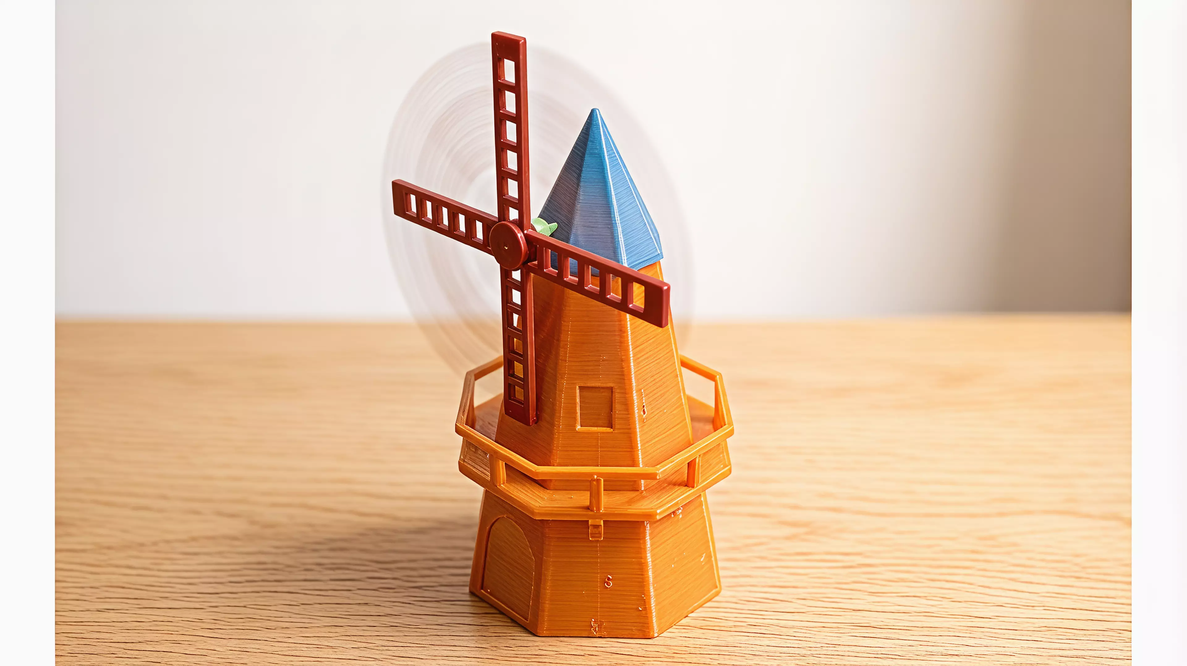 A ~250mm-tall desk windmill tea light holder in a minimal, crisp-edged style: a hollow tapered octagonal tower with an arched candle-access opening, a railed balcony, a conical cap, and a 4-blade lattice sail rotor that spins freely on a brass pin.