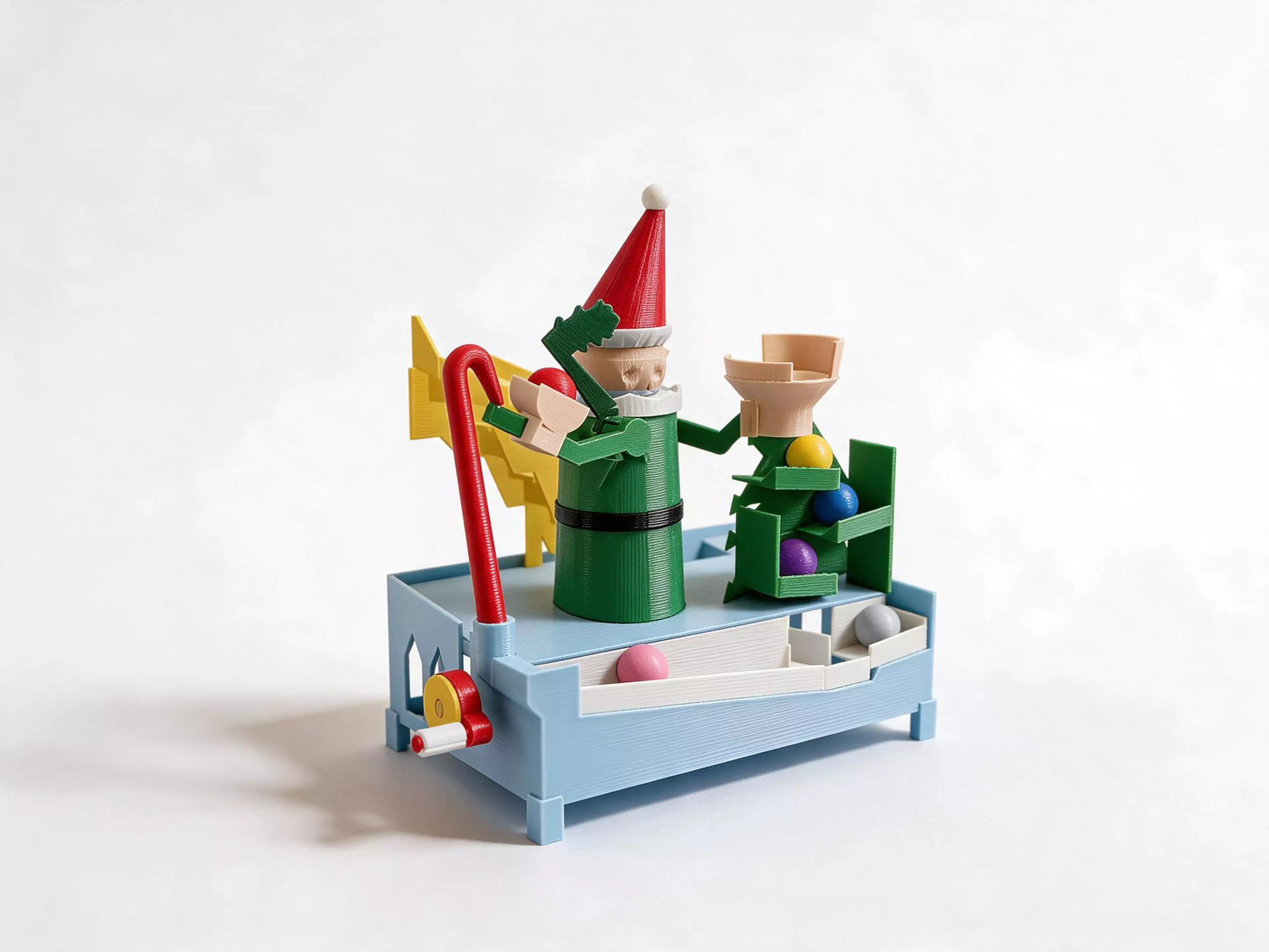 Turn the crank and watch a Christmas elf juggle! Each turn, he tosses a bauble across his face into his mitten. The bauble then rolls down a Christmas tree, along the base, and up a little stair back to his hand, in an endless loop of 10 baubles.