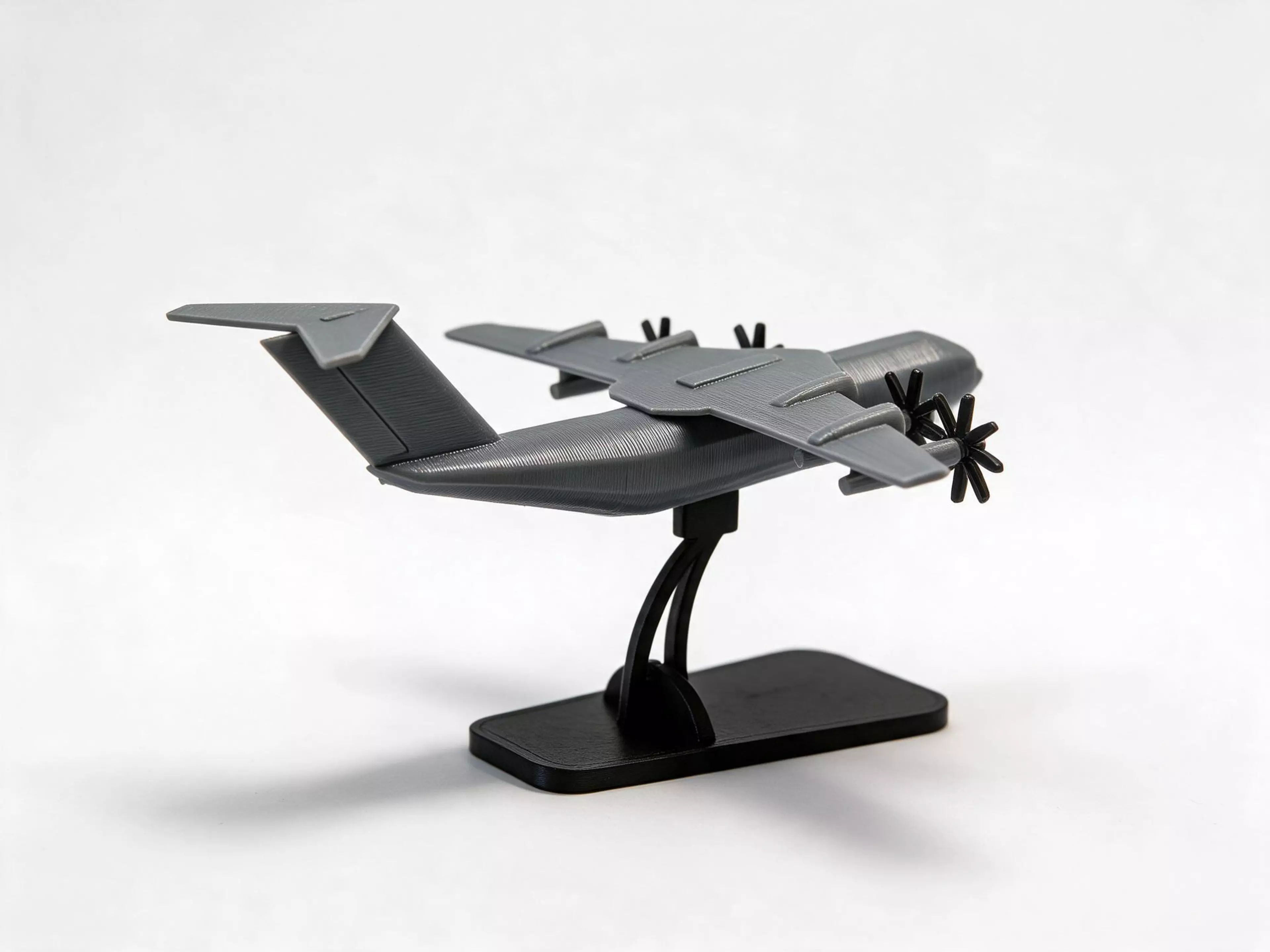 One printed plate. Twenty-one pieces held by a flat sprue web. Twist them free and they assemble into a solid 1:300 Airbus A400M Atlas standing nose-up on an engraved plaque — a lofted fuselage, aerofoil wing and tailplane, four underslung cowls and eight-blade propellers that turn on their axles.