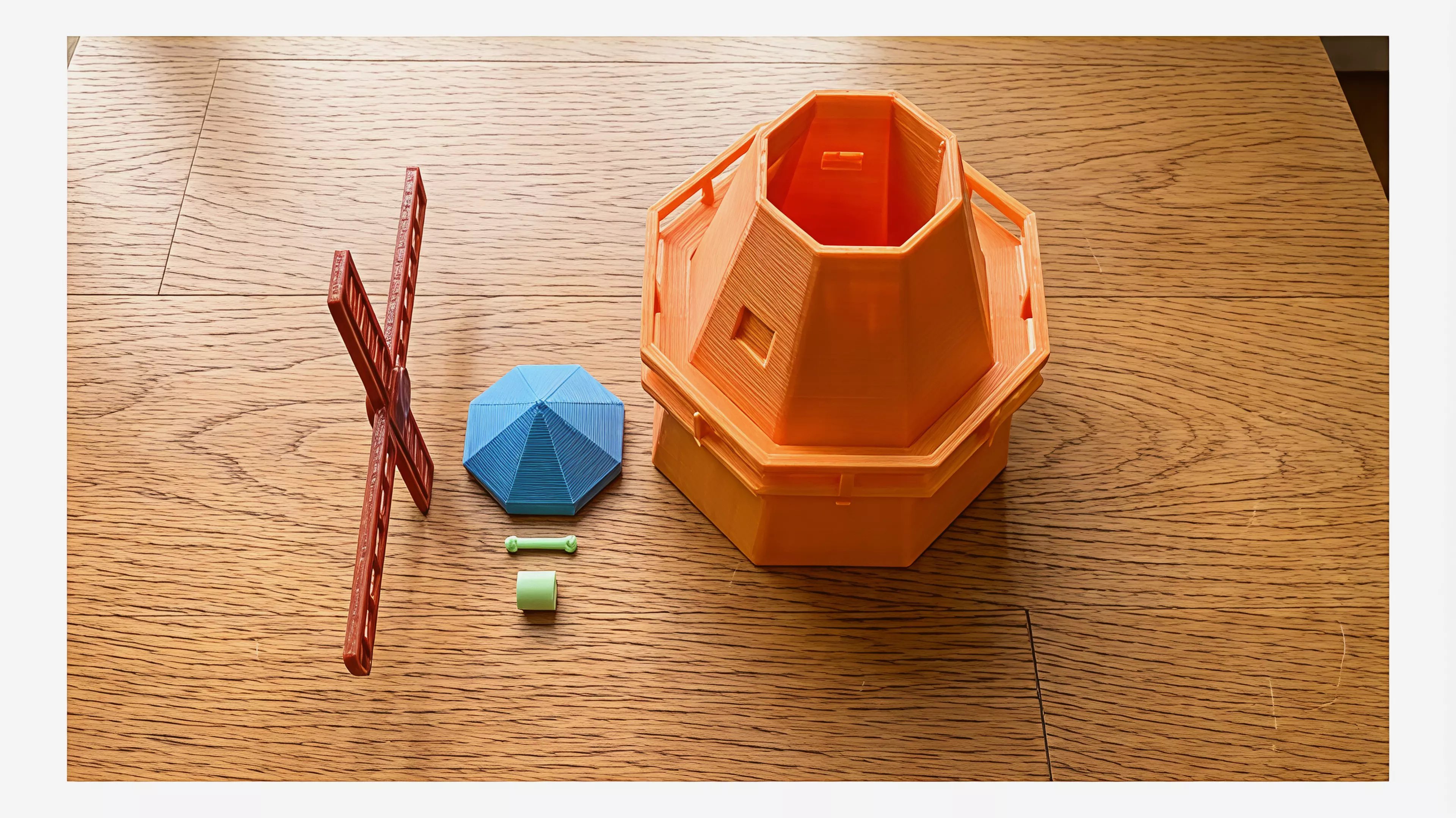 A ~250mm-tall desk windmill tea light holder in a minimal, crisp-edged style: a hollow tapered octagonal tower with an arched candle-access opening, a railed balcony, a conical cap, and a 4-blade lattice sail rotor that spins freely on a brass pin.