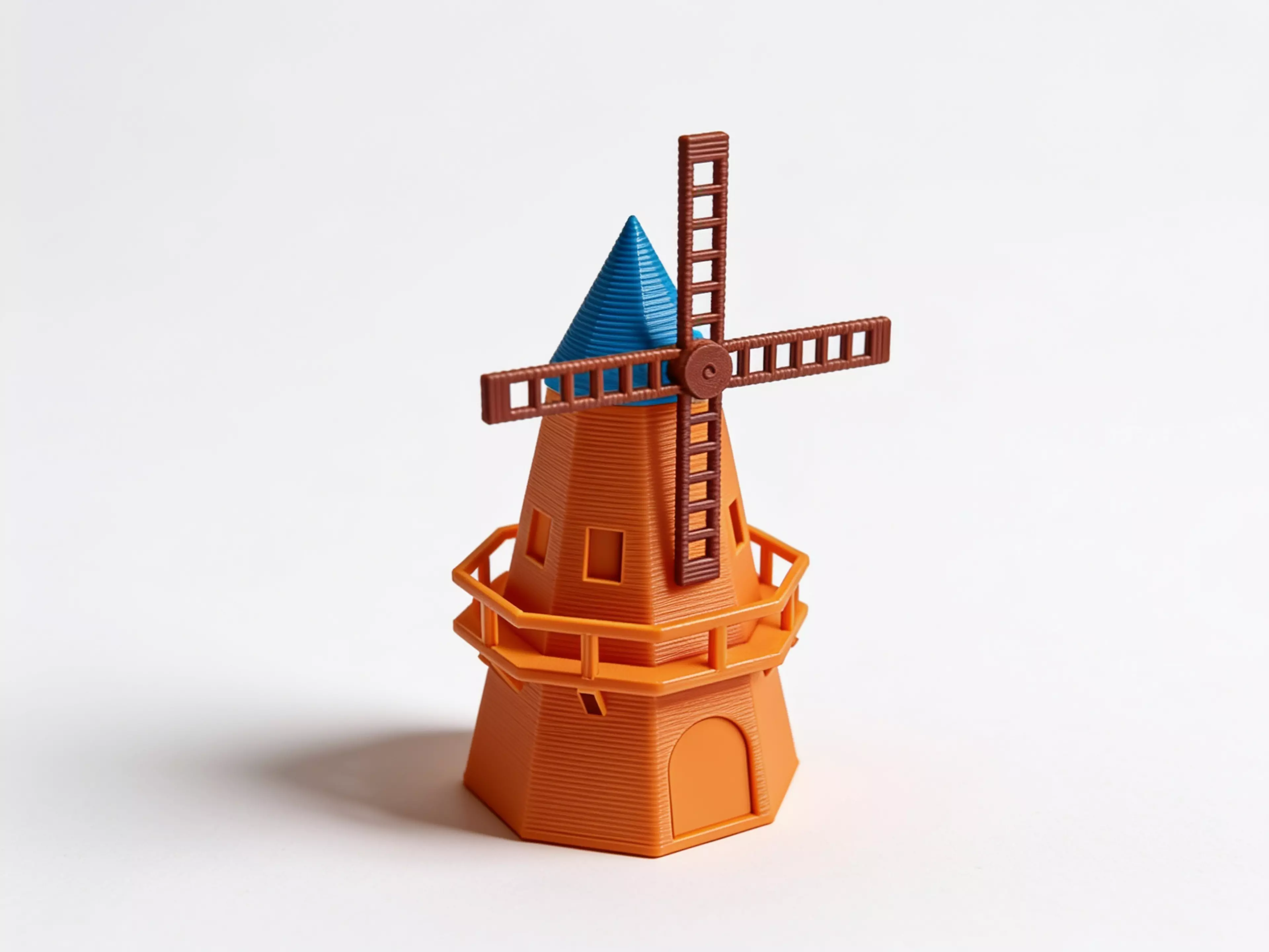 A ~250mm-tall desk windmill tea light holder in a minimal, crisp-edged style: a hollow tapered octagonal tower with an arched candle-access opening, a railed balcony, a conical cap, and a 4-blade lattice sail rotor that spins freely on a brass pin.