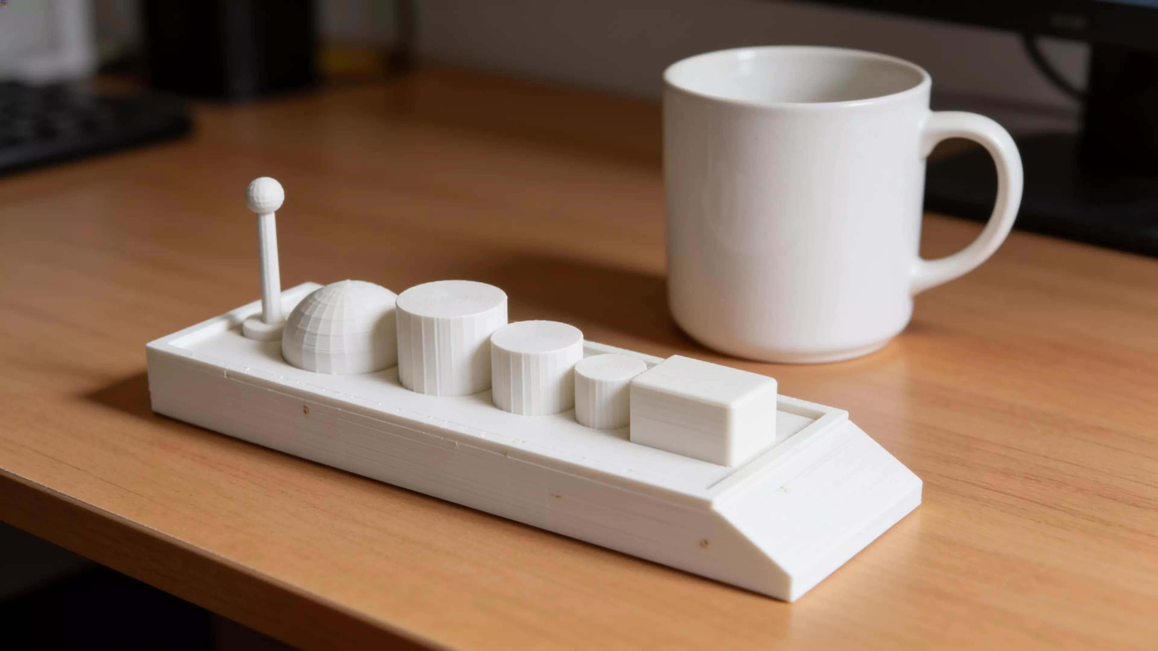 A toy cargo barge — a low, flat-bottomed hull with a raked bow and flat stern — plus six separate deck-cargo pieces (mast/beacon, dome, three drums, and a crate) that peg into sockets on the deck, matching the sketch's assortment.
