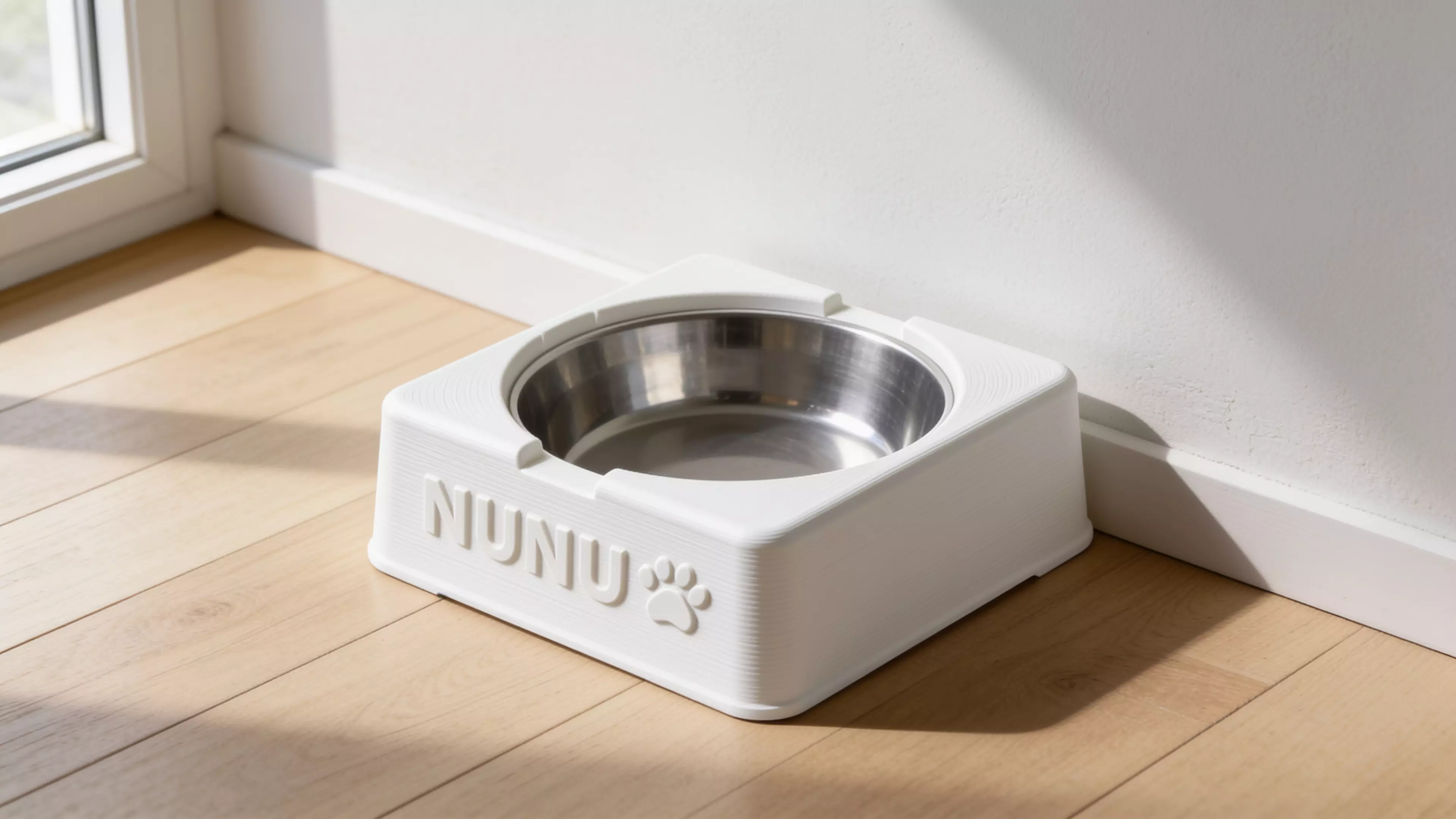 A single-piece, Scandinavian-minimal squircle stand (200 × 200 × 76 mm) that a standard 1-quart stainless bowl drops into from the top and hangs by its rolled rim on an internal support lip, with an anti-spill raised rim, two finger scallops for bowl removal, "NUNU" + paw icon raised on the front…