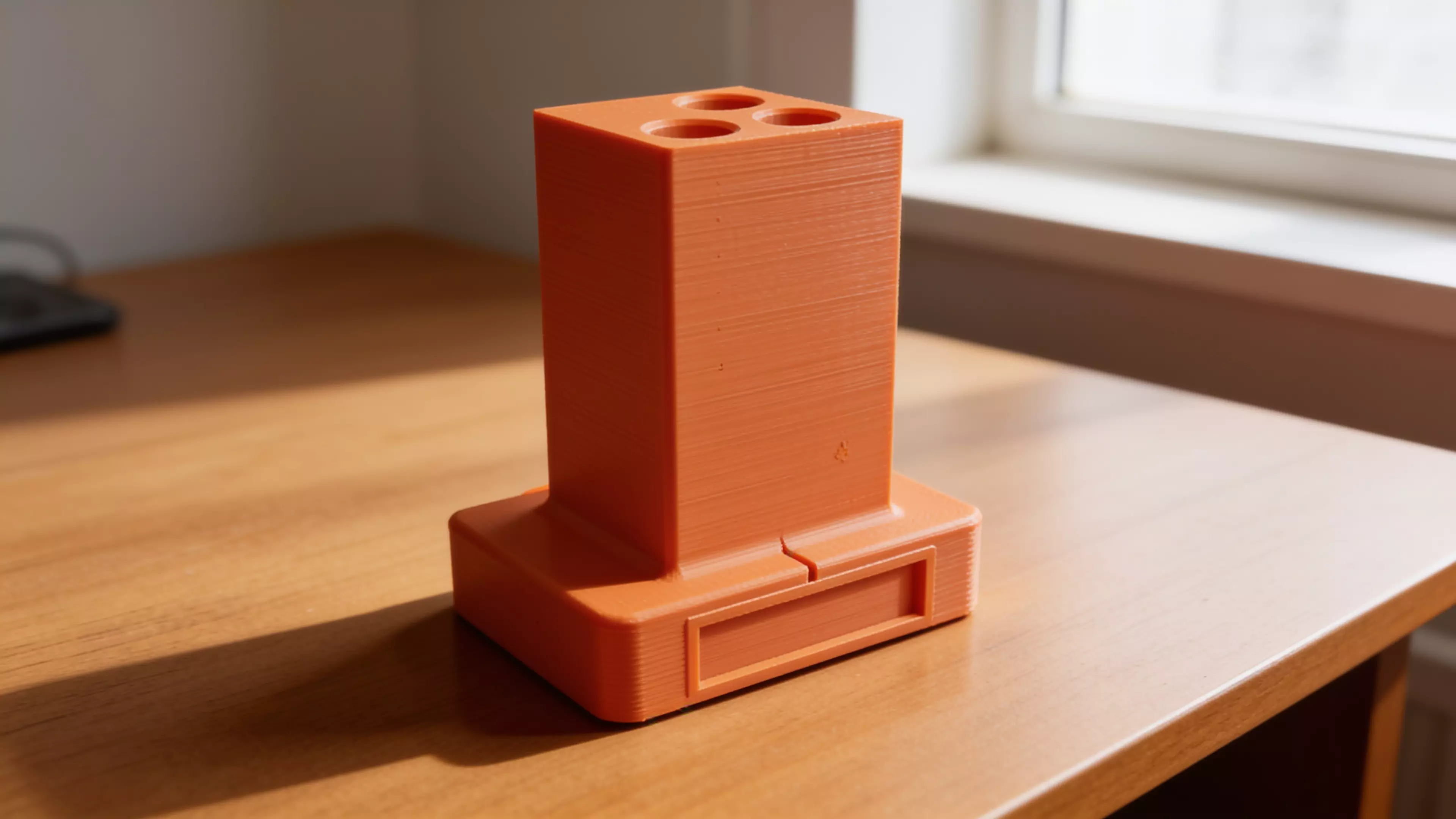 A retro-terminal desk holder: a low, wide CRT-monitor-bezel plinth (complete with a
recessed screen panel and a debossed > prompt) with an oversized rectangular
text-cursor block rising from its top like a frozen "on" blink. Five blind holes
of increasing diameter are drilled into the block's top face in a diagonal,
back-left-to-front-right layout, each sized and chamfered for a specific
implement — stylus, pen, pencil, marker, highlighter. Single piece, flat-bed
print, no supports.