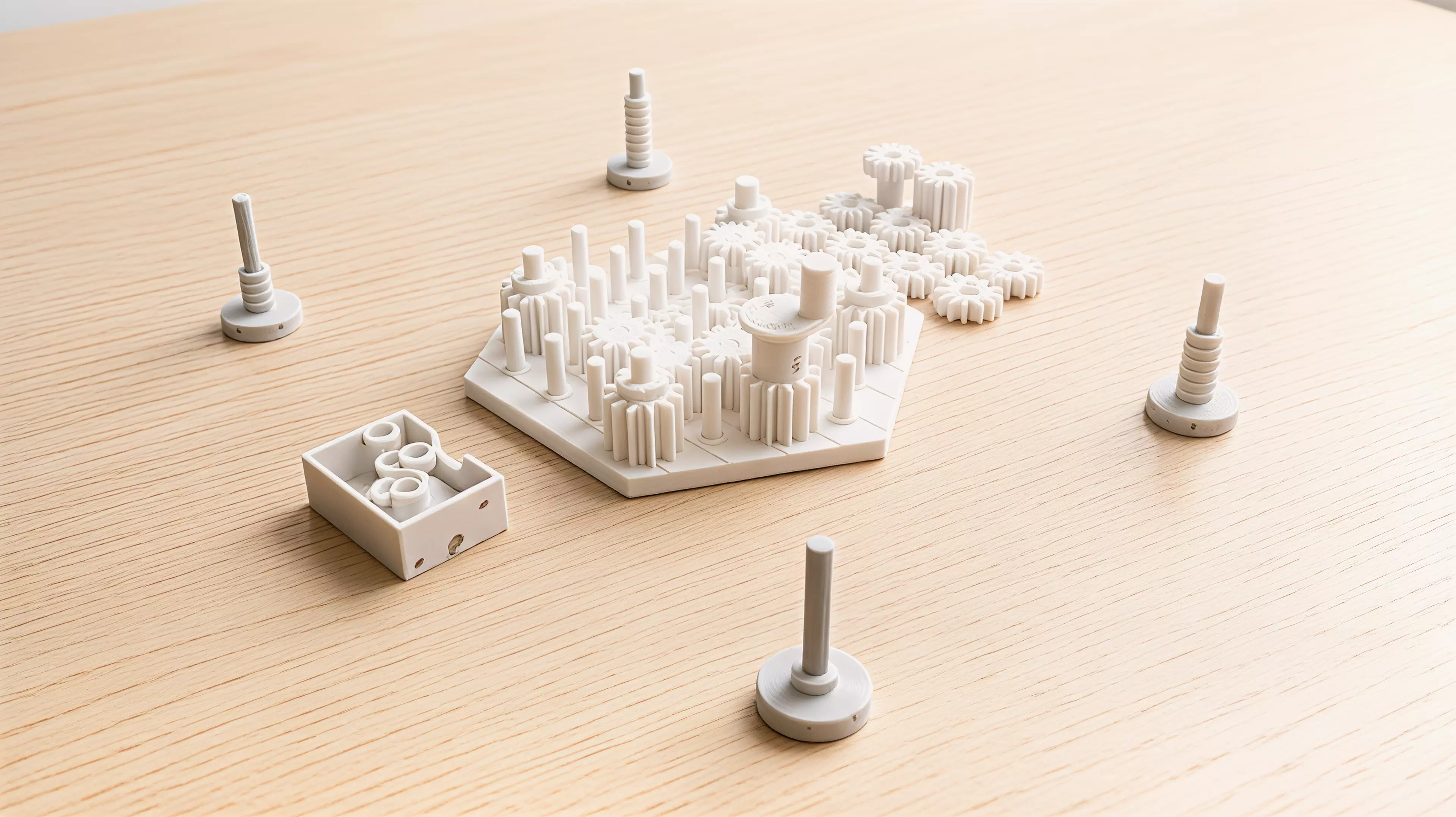 A yard of pins holds real meshing gears, and the game is played inside two facts of engineering: meshed gears turn opposite ways, and a loop with an odd number of them cannot turn at all. Each player owns one furrowed millstone gear standing on the yard's rim; a single crank gear is the only power in the box and it moves to a new rim pin at the start of every round, chosen by whoever leads that round. A turn is placing one gear — low-toothed, high-toothed, or a full-height tandem that bridges both heights — then turning the crank a quarter turn to prove you have not just bound the whole yard solid; at the end of the round the crank goes round once for real and only the mills that come up turning clockwise are grinding.

2-4 players · 35 min