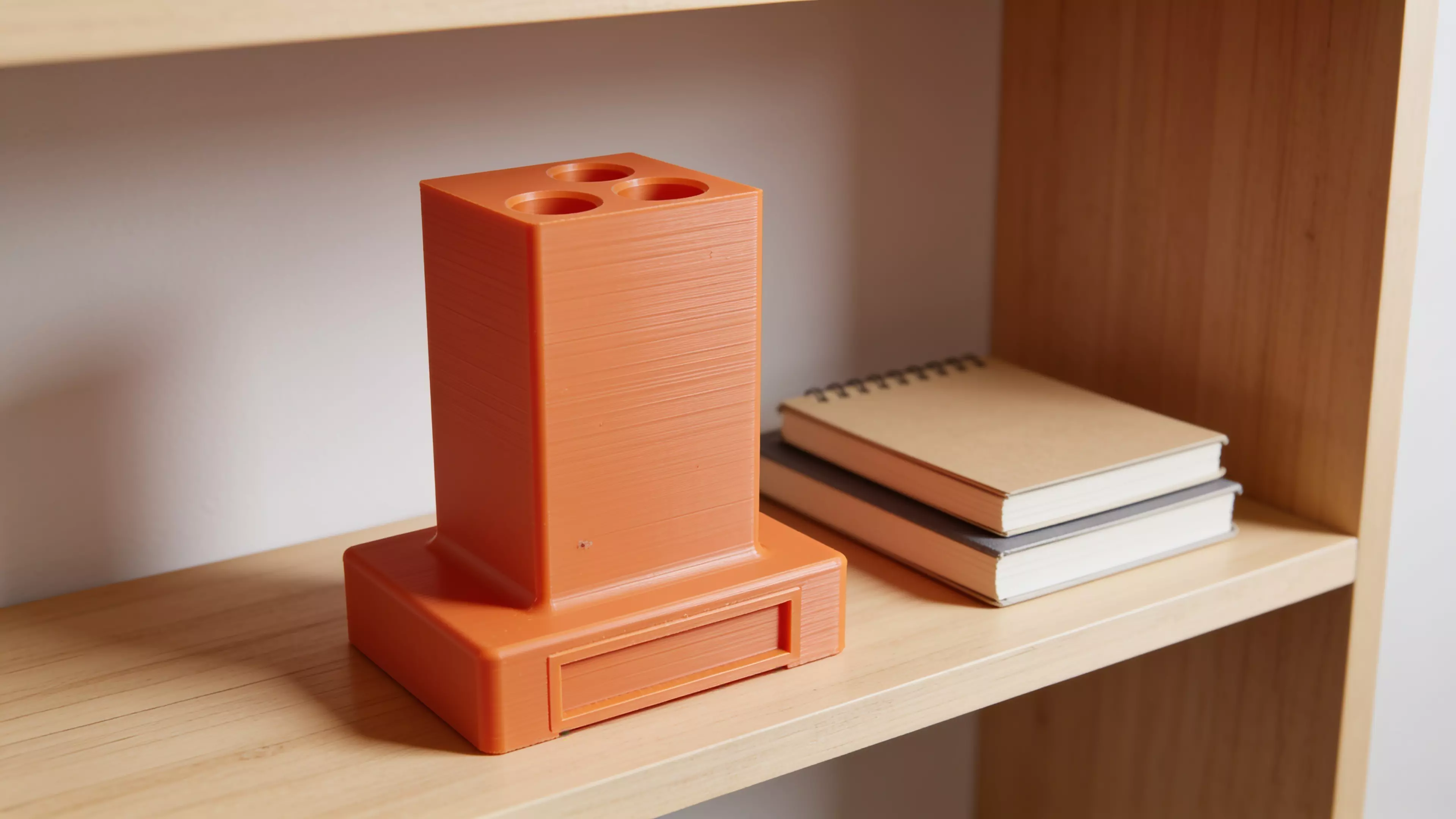 A retro-terminal desk holder: a low, wide CRT-monitor-bezel plinth (complete with a
recessed screen panel and a debossed > prompt) with an oversized rectangular
text-cursor block rising from its top like a frozen "on" blink. Five blind holes
of increasing diameter are drilled into the block's top face in a diagonal,
back-left-to-front-right layout, each sized and chamfered for a specific
implement — stylus, pen, pencil, marker, highlighter. Single piece, flat-bed
print, no supports.