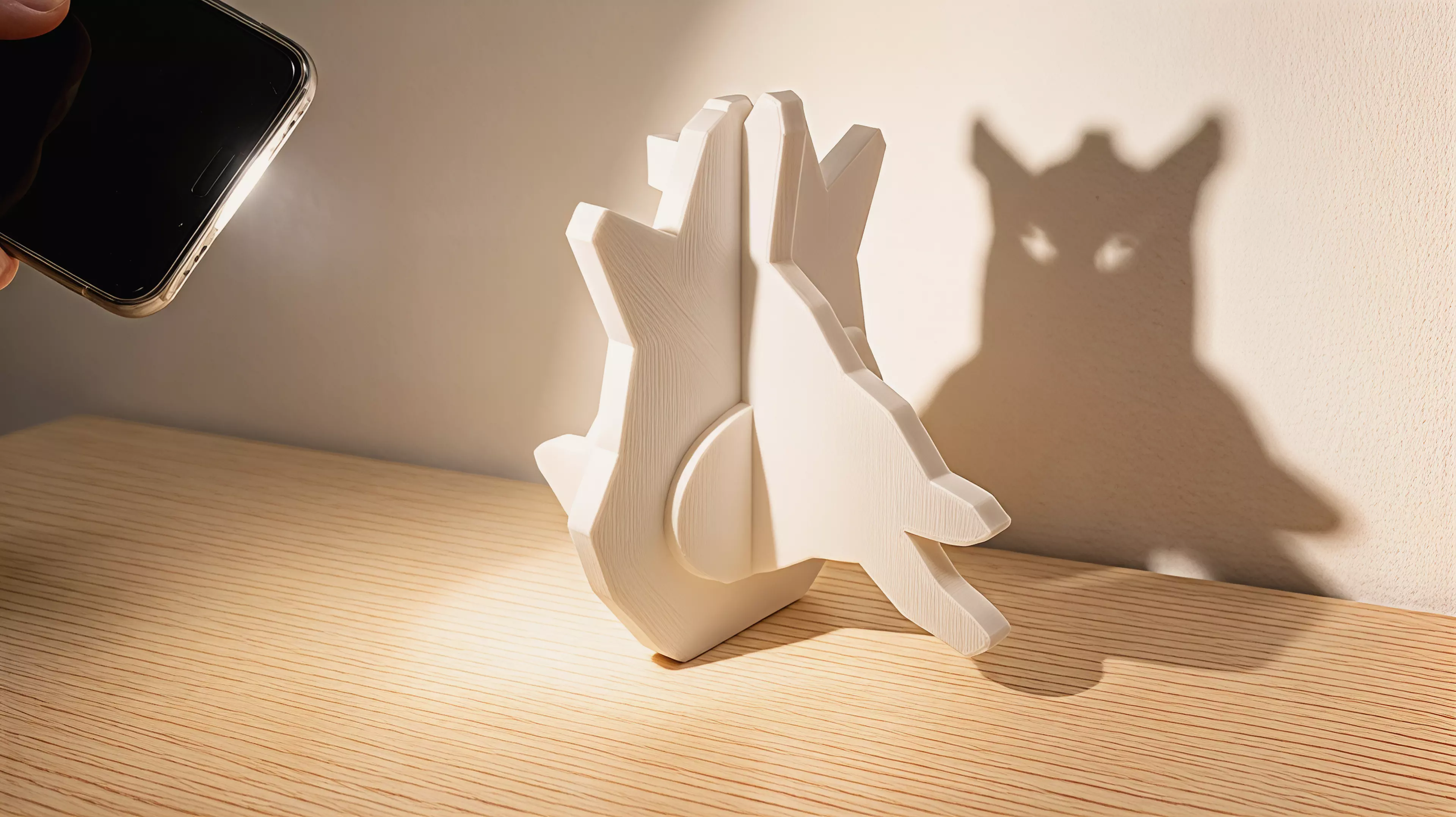 A palm-sized one-piece shadow toy whose broad faces project a horned owl and, after a 90-degree turn, a leaping rabbit under an ordinary external phone flashlight.