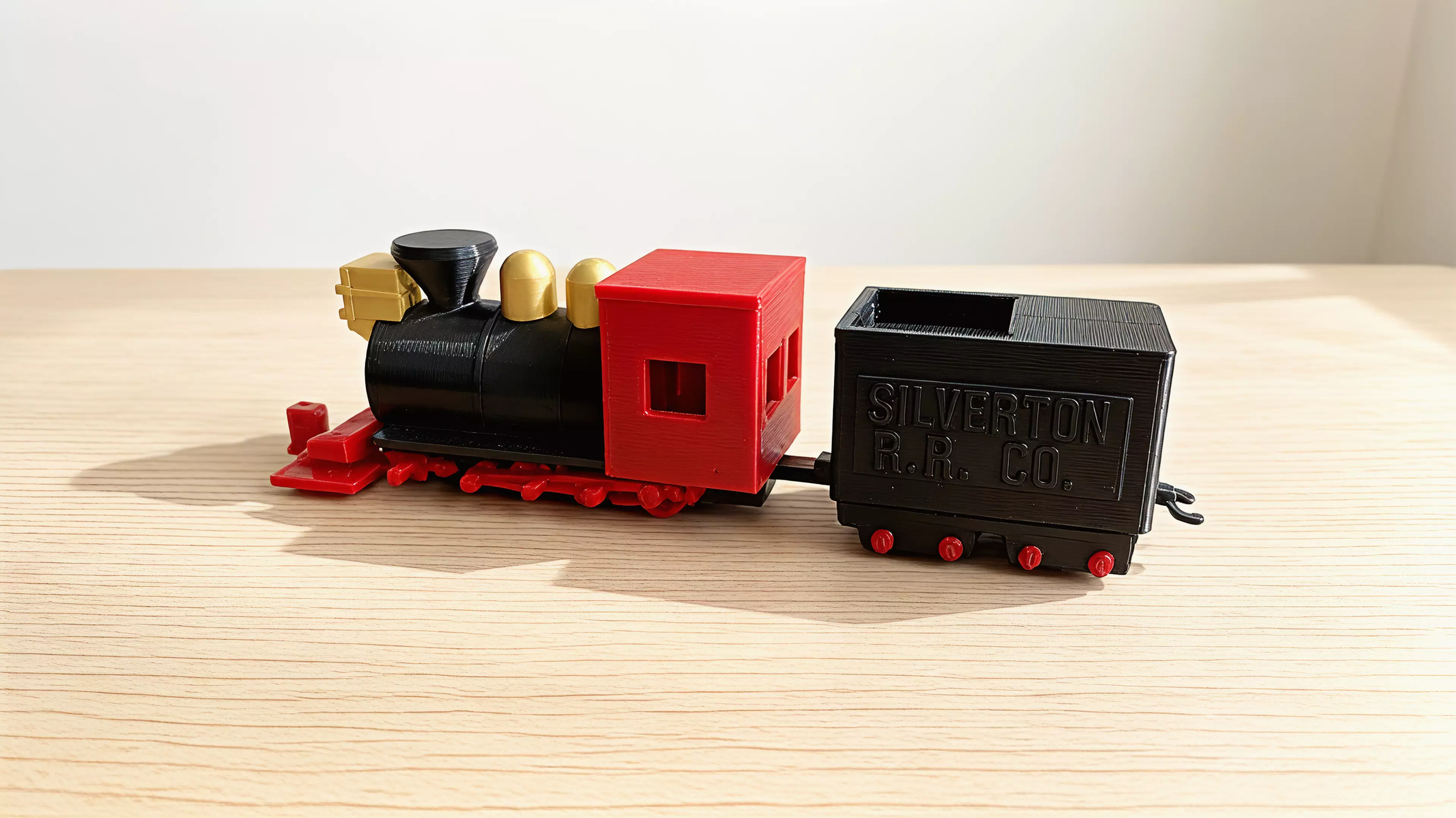 A 1:87 buildable desk model of Silverton Railroad No. 100, with a four-driver 2-8-0 profile, separate rolling wheelsets, a two-truck tender, and a hook-and-bar coupling.