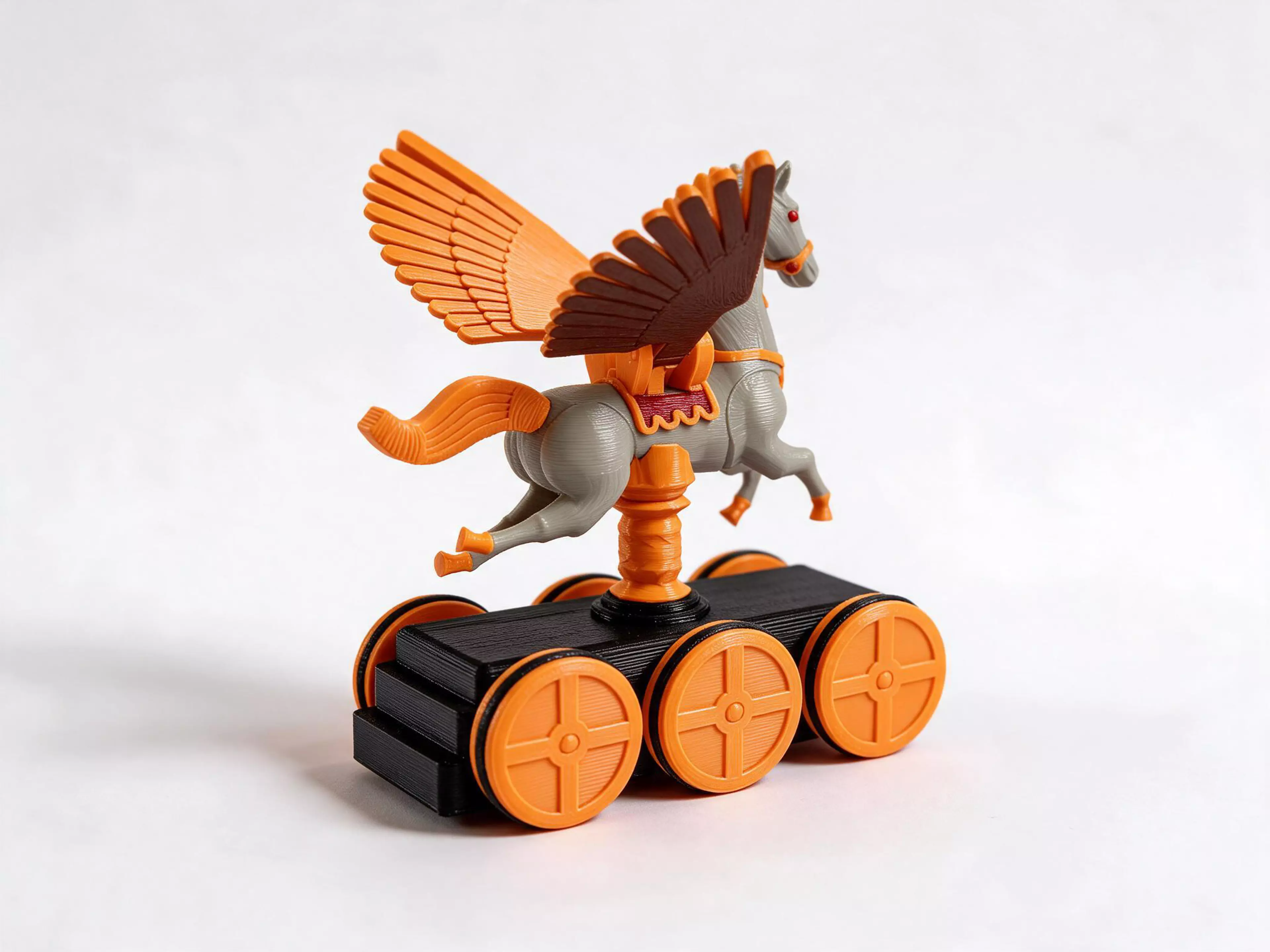 A push-along automaton: a carousel Pegasus, carved, gilded and jewelled like a fairground jumper, flies on a twisted gold pole above a rolling plinth. Push it along the table and every turn of the wheels beats its wings once. 27 printed parts and six O-ring tyres.