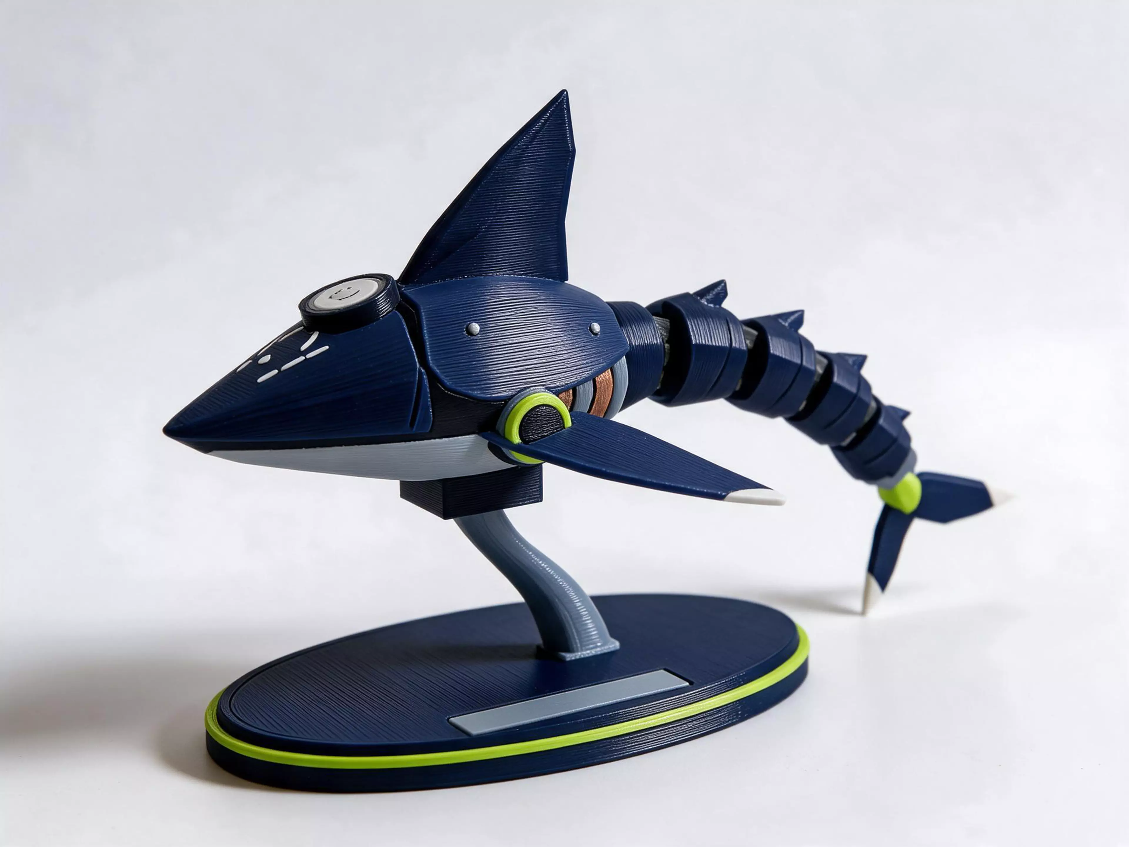 A 250 mm mechanical shark with layered navy armour, lime accents and five ball joints connecting its four tail segments and caudal fin. Eight physical parts assemble into a display model on a removable oval base and support. The pectoral and dorsal fins are fixed to the body. The base plaque is blank, with no raised lettering. Digital CAD prototype: joint fit, retention, friction and durability have not been tested with a physical print.