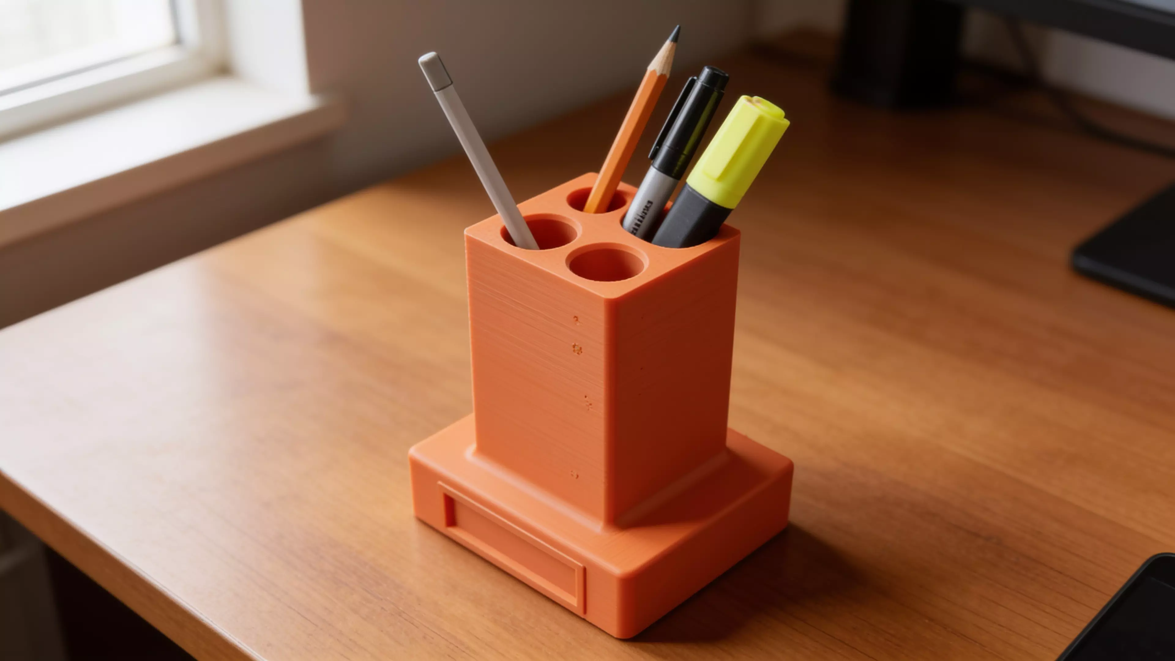 A retro-terminal desk holder: a low, wide CRT-monitor-bezel plinth (complete with a
recessed screen panel and a debossed > prompt) with an oversized rectangular
text-cursor block rising from its top like a frozen "on" blink. Five blind holes
of increasing diameter are drilled into the block's top face in a diagonal,
back-left-to-front-right layout, each sized and chamfered for a specific
implement — stylus, pen, pencil, marker, highlighter. Single piece, flat-bed
print, no supports.