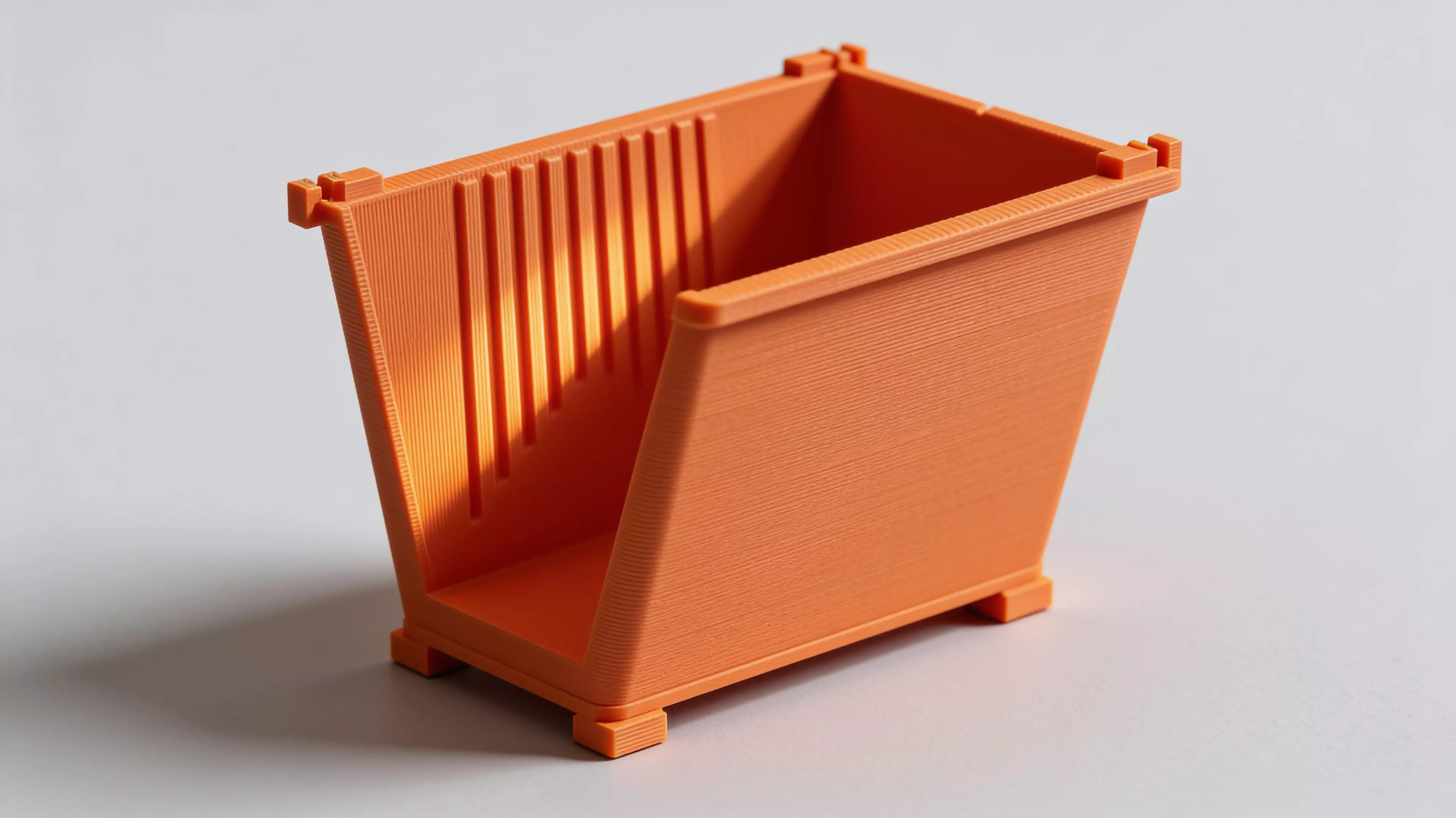 A miniature industrial-dumpster-styled desk trash catcher: a tapered corrugated bin body with two hinged flip lids that meet in the middle, complete with corner skid feet.