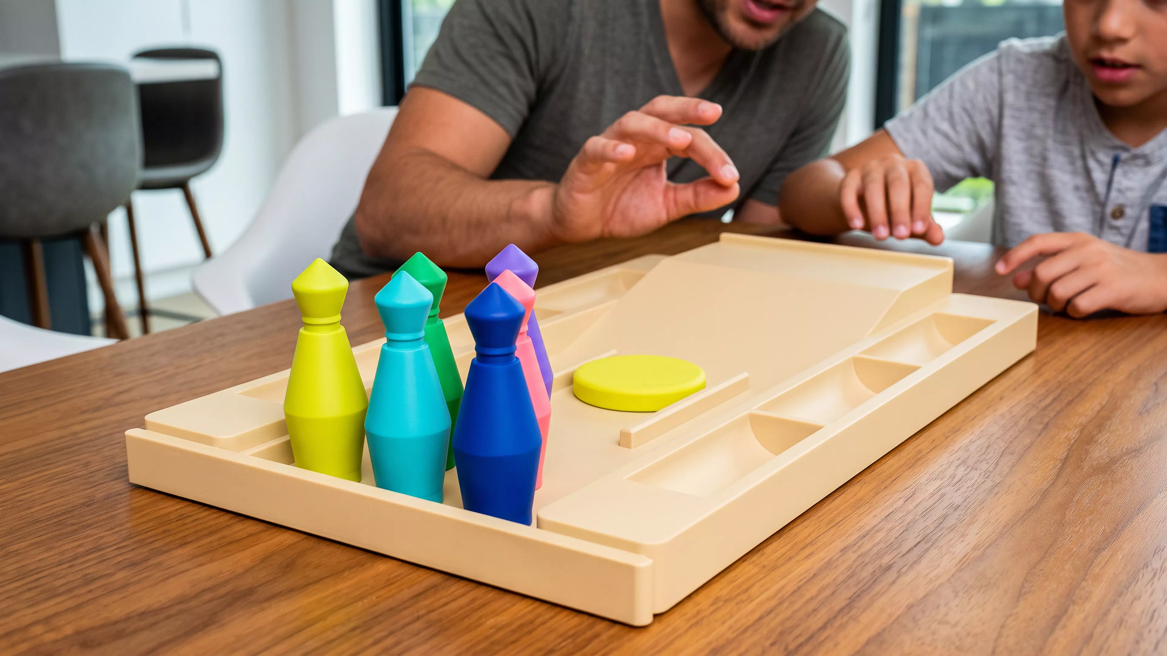 A pocket bowling toy: a lane tray that ramps into a flick-launch pad and doubles as nested storage, six molded pins in a 3-2-1 triangle, and one flick disc — flick the disc off the ramp to send it down the lane into the pins.