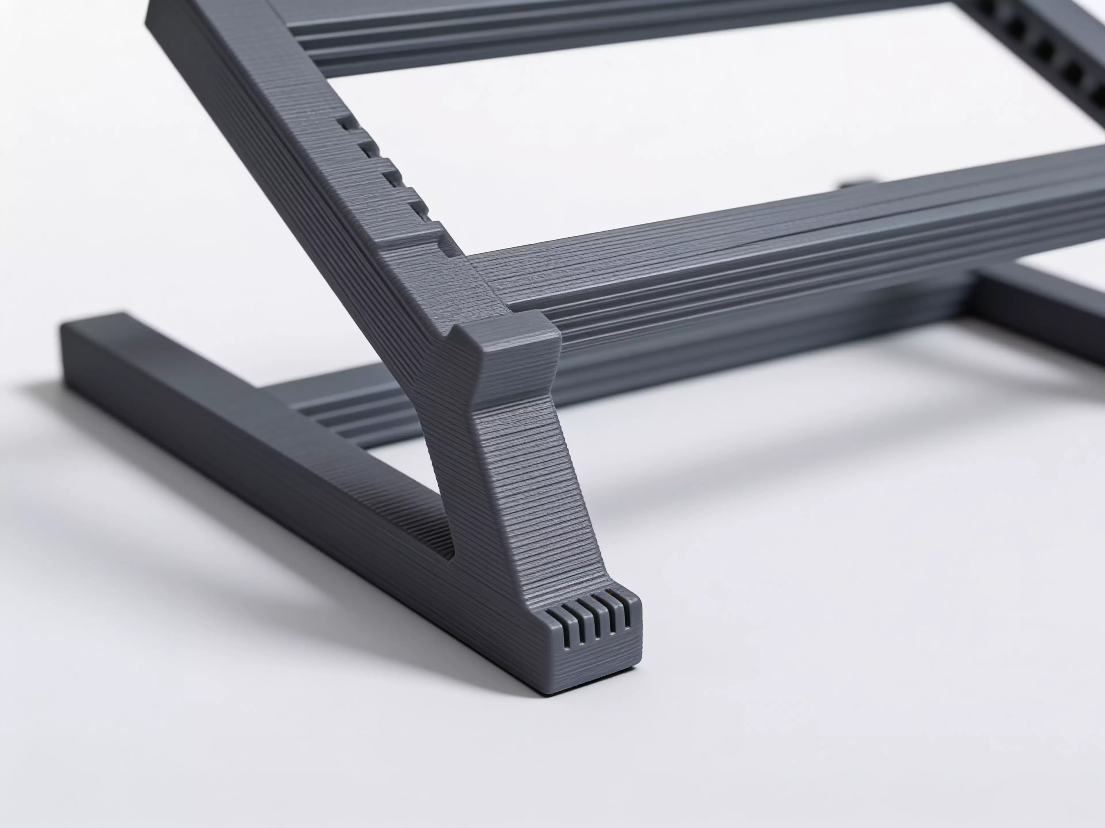 A sculpted Z-profile laptop stand designed around a 13" MacBook, tilted 22° for comfortable typing with a low-profile anti-slip ridge that catches the laptop's front edge. Two mirrored Z-legs — solid where they carry load, hex-relieved where they don't — are braced into a rigid box frame by four I-beam crossbars that press-fit straight into the legs. No screws, no heat-set inserts, no glue: just push the crossbars in and it locks together by friction alone.